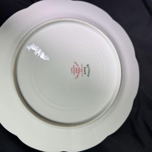 May include: White porcelain plate with a scalloped edge. The underside features a circular design and text in red and green, including "Haviland France" and "Limoges". The plate has a glossy finish and appears to be vintage.