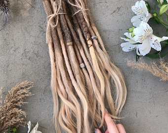 Könnte beinhalten: Ein Set aus synthetischen Dreadlocks mit einem Farbverlauf von dunkelbraun am Ansatz bis hellblond an den Spitzen. Die Dreadlocks sind mit dünnem Garn zusammengebunden und mit kleinen Metallperlen sowie umwickelten Fadenakzenten verziert.