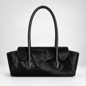 Könnte beinhalten: Eine schwarze Handtasche mit texturierter Felloptik, bestehend aus einem horizontalen, rechteckigen Korpus, einem geschwungenen Klappverschluss und zwei hohen, schmalen, abgerundeten Henkeln, die mit tropfenförmigen Lederlaschen befestigt sind.
