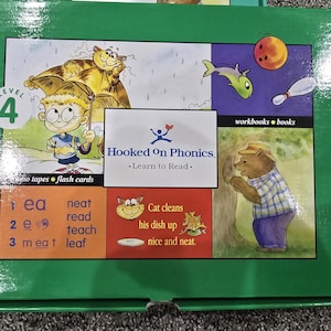 May include: A green Hooked On Phonics Level 4 educational box set featuring illustrations of a child with a cat under an umbrella, a bear, and a bowling ball. The box includes text such as Hooked On Phonics, Learn to Read, and phonics word lists.