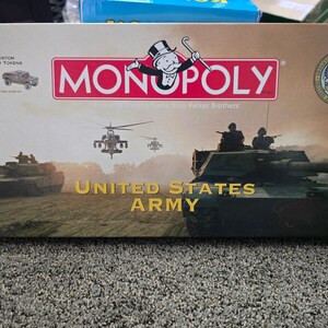 Könnte beinhalten: Eine Monopoly United States Army Edition Brettspielschachtel mit einer braunen und beigen Landschaft mit Militärpanzern und Hubschraubern. Die Schachtel zeigt das Monopoly-Logo, das Siegel der US-Armee und sechs individuelle Zinn-Spielfiguren.