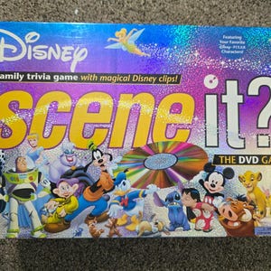 Può includere: Una scatola del gioco da tavolo Disney Scene It? DVD con finitura olografica. La copertina presenta il titolo in grandi lettere gialle e bianche, una grafica centrale del disco DVD e vari personaggi Disney tra cui Topolino, Buzz Lightyear e Pippo.