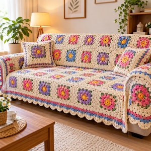Può includere: Un copridivano all'uncinetto color crema con un motivo ripetuto a piastrelle granny e centri floreali nei toni del rosa, viola, giallo e blu. Il copridivano include due cuscini quadrati abbinati e un bordo decorativo smerlato.