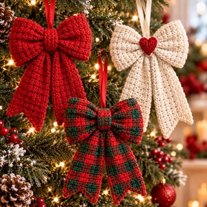 May include: Three handmade crochet bow ornaments hanging on a Christmas tree. One bow is solid red, one is cream-colored with a small red heart in the center, and one features a red and dark green plaid pattern. Each has a ribbon loop.