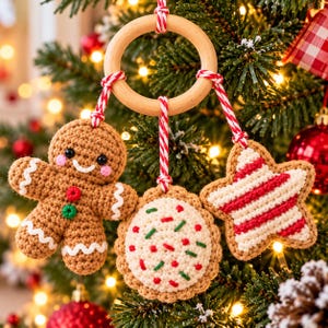 Op de afbeelding: Een houten ring met drie gehaakte hangers: een bruin peperkoekmannetje met roze wangen, een rond koekje met rode en groene spikkels, en een ster met rode en witte strepen, allemaal opgehangen aan een rood-wit touwtje.