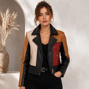 Puede incluir: Una chaqueta estilo motero con bloques de color en negro, marrón claro, crema y rojo. La chaqueta presenta un cuello de solapa ancho, mangas largas y cierre de cremallera frontal. Se lleva sobre una parte superior y pantalones de color negro.