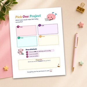 Op de afbeelding: Een wit takenplanningsblad getiteld Pick One Project met een cartoonbrein achter een laptop. Het bevat vier gekleurde vakken met de labels A, B, C en D, een sectie om taken te elimineren met een axolotl-illustratie en een vak voor de Chosen One taak.