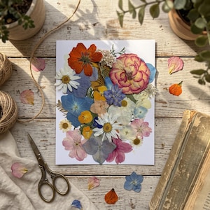 May include: A rectangular white card featuring a collage of pressed dried flowers in various colors including orange, pink, blue, white, and yellow. The arrangement includes daisies, hydrangea petals, and rose blooms, creating a dense floral display.