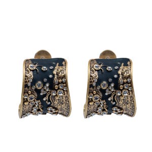 May include: A pair of hoop earrings featuring a wide, curved design with a dark charcoal enamel finish. The surface is accented with textured, antiqued gold-tone metal detailing and embedded with numerous small, clear, round-cut crystals.