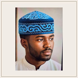 Puede incluir: Un casquete azul oscuro con intrincados patrones bordados en azul claro y blanco en la corona y una banda horizontal. El bordado consiste en motivos de remolinos repetitivos que envuelven toda la circunferencia de la prenda.