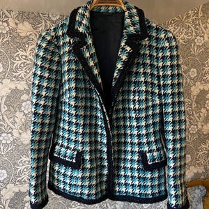 Può includere: Un blazer con motivo pied-de-poule nei toni del verde acqua, blu navy e bianco. Il capo presenta un bordo testurizzato blu navy scuro lungo i revers, i polsini e le due tasche frontali con patta. È foderato con un tessuto blu navy scuro.