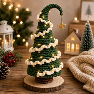 May include: A dark green crocheted Christmas tree with a curved top, decorated with a white wavy yarn garland, small gold beads, and integrated warm white fairy lights. A gold star ornament hangs from the tip, set on a round wooden base.