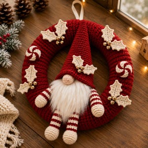 May include: A circular red crocheted wreath featuring a central gnome with a tall red hat, a white faux fur beard, and striped arms and legs. The wreath is decorated with crocheted cream-colored holly leaves, small gold beads, and red and white swirls.