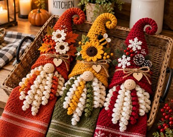 May include: Three crocheted gnome-themed hanging kitchen towels in a wicker basket. The left towel is orange with autumn leaves and flowers. The centre towel is green with a sunflower and bee. The right towel is red with snowflakes and pinecones.