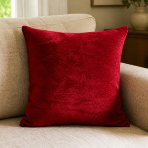 Puede incluir: Una funda de cojín cuadrada de color rojo intenso y vibrante. La tela tiene un aspecto suave, texturizado y aterciopelado con un brillo sutil que capta la luz, creando variaciones en la intensidad del tono rojo por toda la superficie.