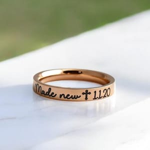 May include: A gold-toned ring with the inscription "Made new + 11:20" engraved on the band.