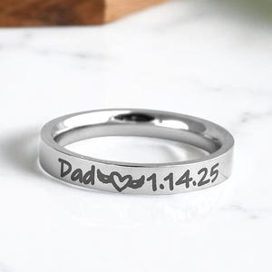 以下が含まれることがあります： 「Dad」とハートマーク、それに続く日付「1.14.25」が刻まれた銀の指輪。