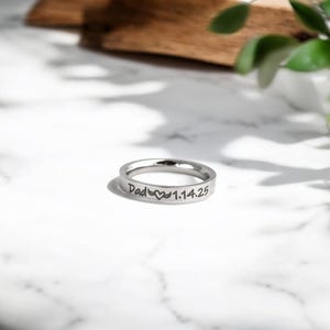 May include: A silver ring with the inscription "Dad" followed by a heart symbol and the date "1.14.25".
