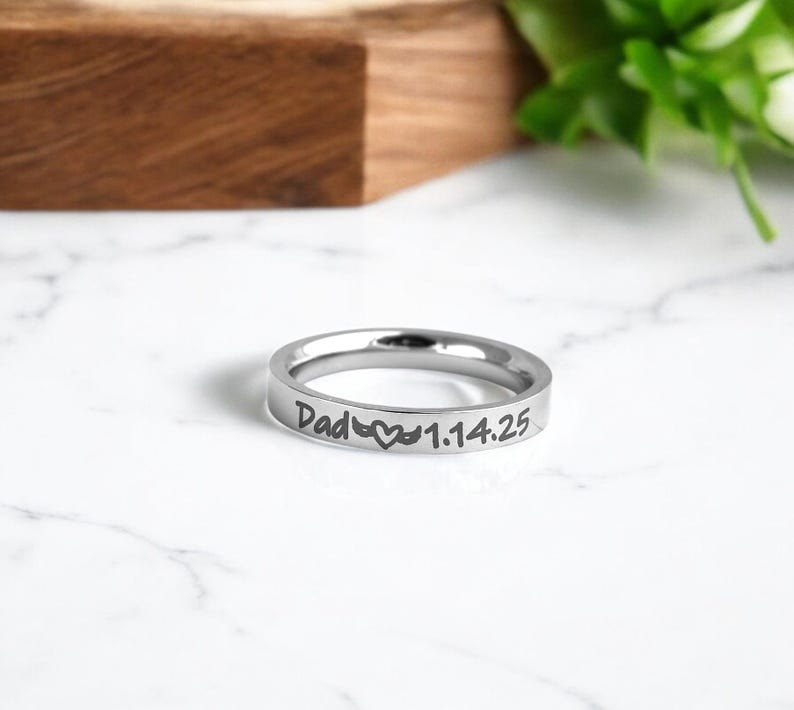 May include: Silver ring with the inscription "Dad" and a heart symbol, followed by the date "1.14.25".
