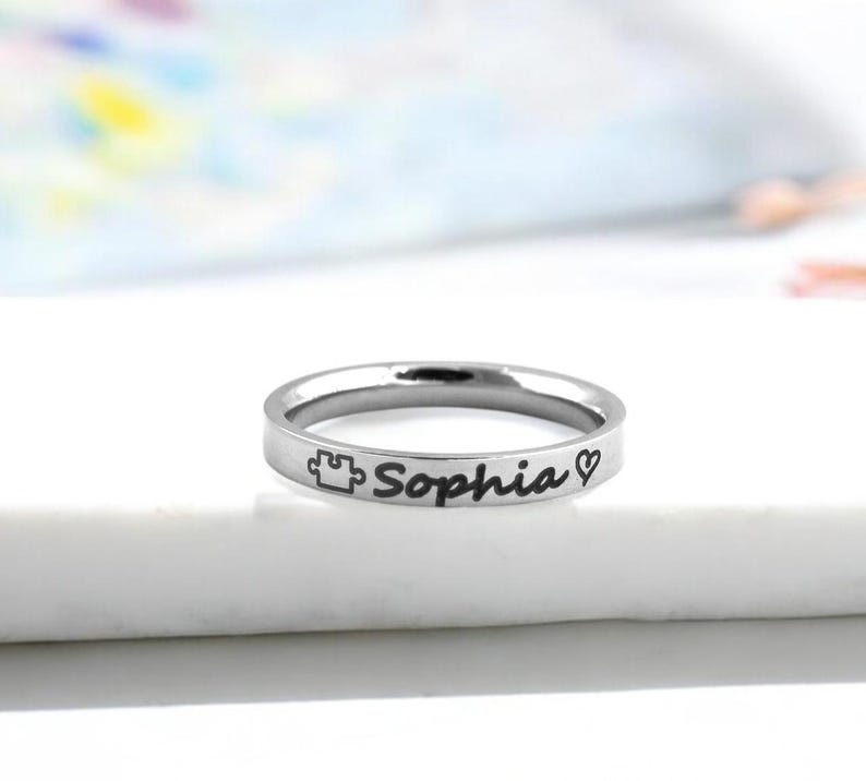 Pode incluir: Um anel de prata com o nome "Sophia" gravado, juntamente com uma pe&ccedil;a de quebra-cabe&ccedil;a e um s&iacute;mbolo de cora&ccedil;&atilde;o.