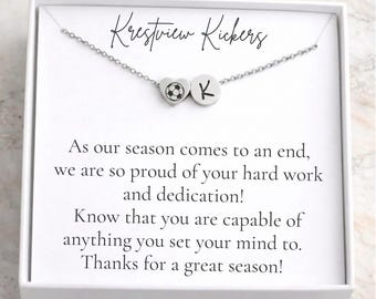 Könnte beinhalten: Eine silberne Halskette mit einem herzförmigen Anhänger mit einem Fußballmotiv und einem runden Anhänger mit dem Buchstaben "K". Die Kette wird auf einer weißen Karte mit dem Text "Krestview Kickers" und einer motivierenden Botschaft präsentiert.