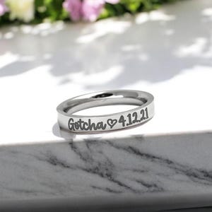 May include: A silver ring with the inscription "Gotcha ♥ 4.12.21" engraved on the band.