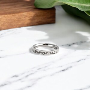 May include: A silver ring with the inscription "Dad" followed by a heart symbol and the date "1.14.25".