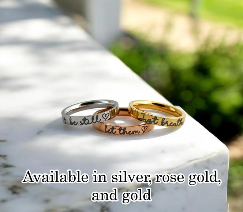 May include: Three thin stacking rings with engraved messages: "+ be still", "let them", and "Just breathe". Available in silver, rose gold, and gold.
