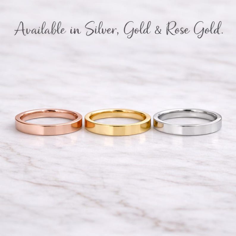 Może przedstawiać: Trzy pierścionki w kolorze r&oacute;żowego złota, złota i srebra, prezentowane na marmurowej powierzchni. Pierścionki to proste obrączki o płaskim designie. Tekst u g&oacute;ry brzmi "Available in Silver, Gold & Rose Gold."