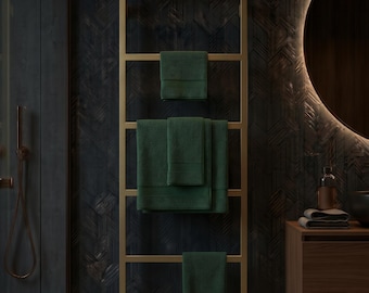 May include: A rectangular gold-toned metal towel rack mounted vertically, featuring five horizontal bars. Three dark green textured towels are draped over the rack, with one small towel on the top bar, a larger folded towel in the middle, and one small towel on the bottom bar.