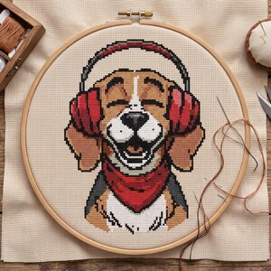 May include: A cross-stitch embroidery project in a wooden hoop featuring a beagle dog wearing red headphones and a red bandana. The design is stitched onto light beige Aida fabric, showcasing a smiling dog with brown and white fur.