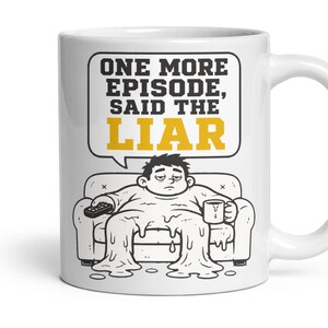 May include: A white ceramic mug featuring a black and white line drawing of a person melting into a sofa while holding a remote and a mug. Above the figure is a speech bubble with the text "ONE MORE EPISODE, SAID THE LIAR" in black and yellow.