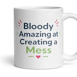 May include: A white ceramic mug featuring the dark blue text Bloody Amazing at Creating a, with the word Mess in light green below it. The design includes small red accent marks and a small pink heart centred beneath the text on the mug.
