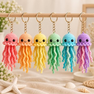 May include: Six crochet jellyfish keychains hanging in a row, each featuring a round head, dangling curly tentacles, and two black bead eyes. The jellyfish are coloured pink, orange, yellow, light green, blue, and purple, each with a gold metal ring.