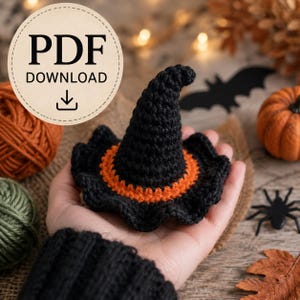 May include: A small, hand-crocheted witch hat featuring a pointed black crown and a wide, wavy black brim accented with a vibrant orange band at the base. The image includes a circular badge with the text PDF DOWNLOAD and a download icon.