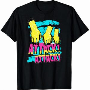 May include: A black short-sleeved t-shirt featuring a graphic of three severed yellow hands reaching downwards. Behind the hands are horizontal cyan brush strokes. Below the hands, the text ATTACK! ATTACK! is printed in bold pink letters.