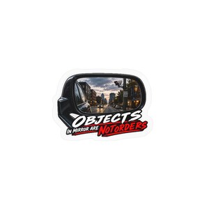 Puede incluir: Una pegatina troquelada que muestra un espejo lateral de coche negro que refleja una calle urbana al atardecer. Debajo del espejo, el texto "OBJECTS IN MIRROR ARE NOT ORDERS" aparece en letras blancas y rojas, con un borde blanco alrededor.