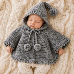 Peut inclure: Une cape à capuche crochetée grise pour nourrisson, dotée d'une capuche pointue avec un pompon au sommet, d'une fermeture à nouer avec deux pompons et d'un bord festonné décoratif sur l'ourlet et les manches, portée sur un legging crème.