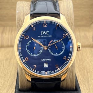 Könnte beinhalten: Eine IWC Schaffhausen Automatikuhr mit goldfarbenem Gehäuse, tiefblauem Zifferblatt und schwarzem Lederarmband. Das Zifferblatt zeigt goldfarbene Ziffern, zwei Hilfszifferblätter, ein Datumsfenster auf der Sechs-Uhr-Position und IWC Schaffhausen.
