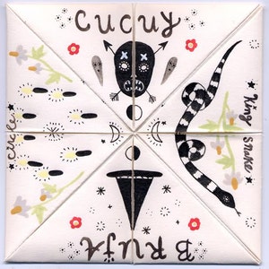 May include: A white, folded paper fortune teller with hand-drawn illustrations and text. The design includes a black skull, a black and white snake, flowers, and the words "Cucuy", "Circle", "King Snake", and "Bruja".