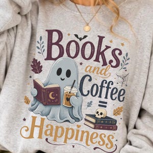 Könnte beinhalten: Ein hellgraues Sweatshirt mit Rundhalsausschnitt und einem Aufdruck eines Geistes, der ein offenes Buch und einen Kaffeebecher hält. Der Text lautet Books and Coffee = Happiness. Ergänzt durch einen kleinen Totenkopf auf Büchern, Blätter und Sterne.