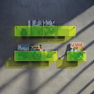 Könnte beinhalten: Drei horizontale Wandregale aus durchscheinendem, neongelbem Acryl. Die Regale sind an beiden Enden mit silberfarbenen, kreisförmigen Beschlägen befestigt. Verschiedene Bücher und Zeitschriften stehen aufrecht in den Regalen und werfen Schatten.