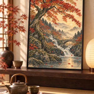 Peut inclure: Une impression d'art encadrée représentant un paysage avec un grand érable aux feuilles d'automne rouge et orange vif, une cascade s'écoulant sur des rochers moussus, un pont en pierre et des montagnes lointaines sous un ciel doux.