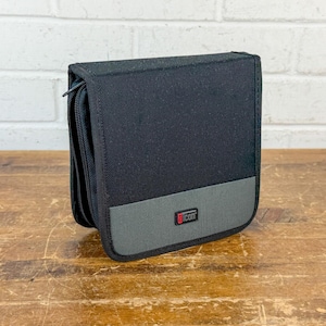 May include: A black and gray rectangular storage case with a zippered closure. The case features a textured black fabric upper section and a smooth gray lower panel with a small rectangular logo tag that reads icon in white text.