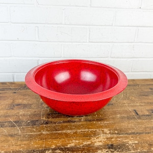 May include: A round, deep mixing bowl with a vibrant red finish and a subtle black speckled pattern throughout the surface. The bowl features a wide, flat rim and a smooth, curved interior, providing a consistent color and texture.