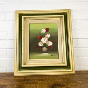 May include: A framed painting of a bouquet of white and red flowers in a vase. The flowers are painted in a realistic style and the background is a green.