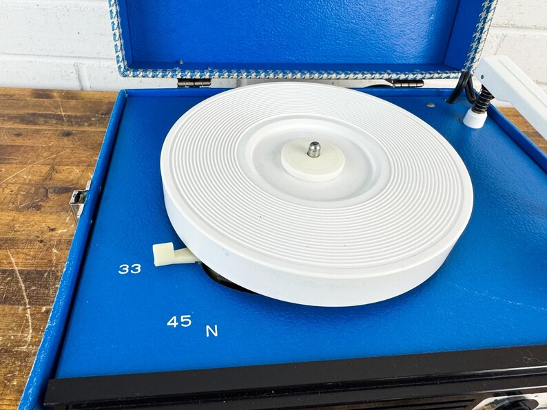 May include: A vintage blue record player with a white turntable. The player has a black front panel and a blue lid with a patterned trim. The speed settings 33 and 45 are visible.
