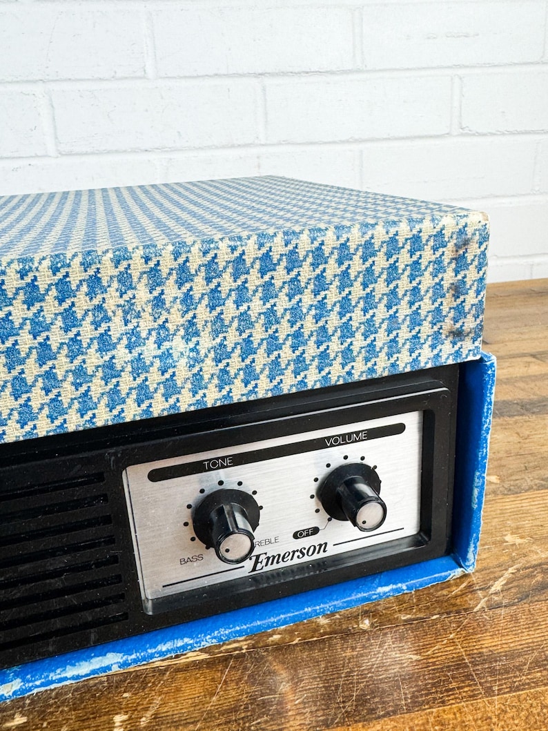 May include: Vintage Emerson radio with a blue and white houndstooth patterned top. The radio has a black face with silver controls for tone and volume. The brand name "Emerson" is printed on the face.