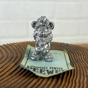May include: A silver pewter figurine of a lion with a beard and a mane. The figurine is sitting on a green card with the text "Handcast Pewter Deewee".