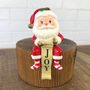 クリスマス用のヴィンテージサンタクロースストッキングホルダー。喜びのバナーを持つサンタ。樹脂製ストッキングハンガー。